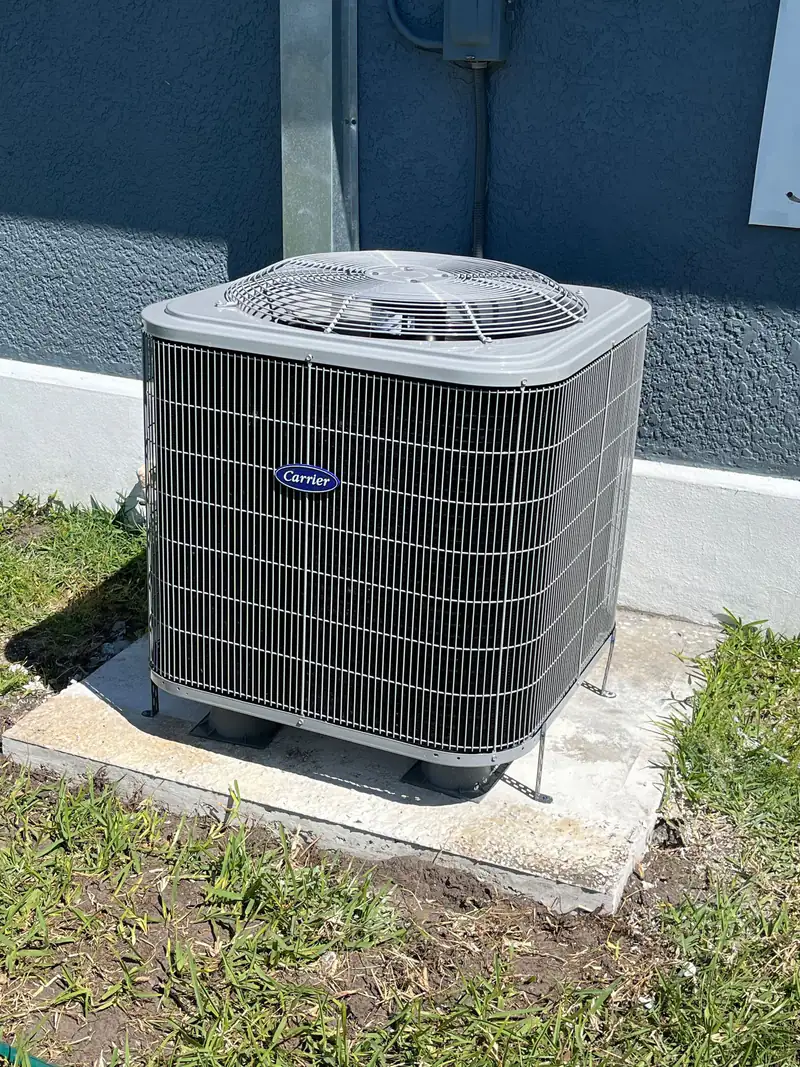 New Carrier condenser on a concrete pad beside a blue stucco house