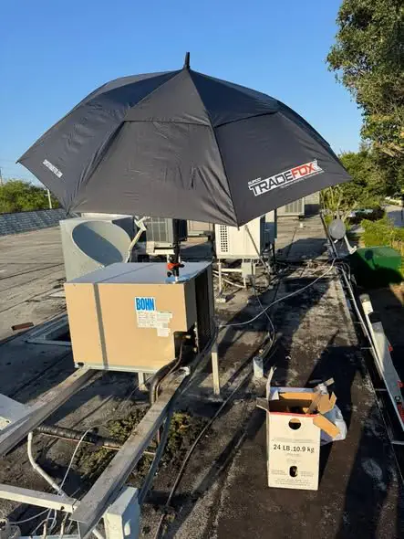 Rooftop unit opened for service under a shade umbrella, refrigerant cylinder beside it